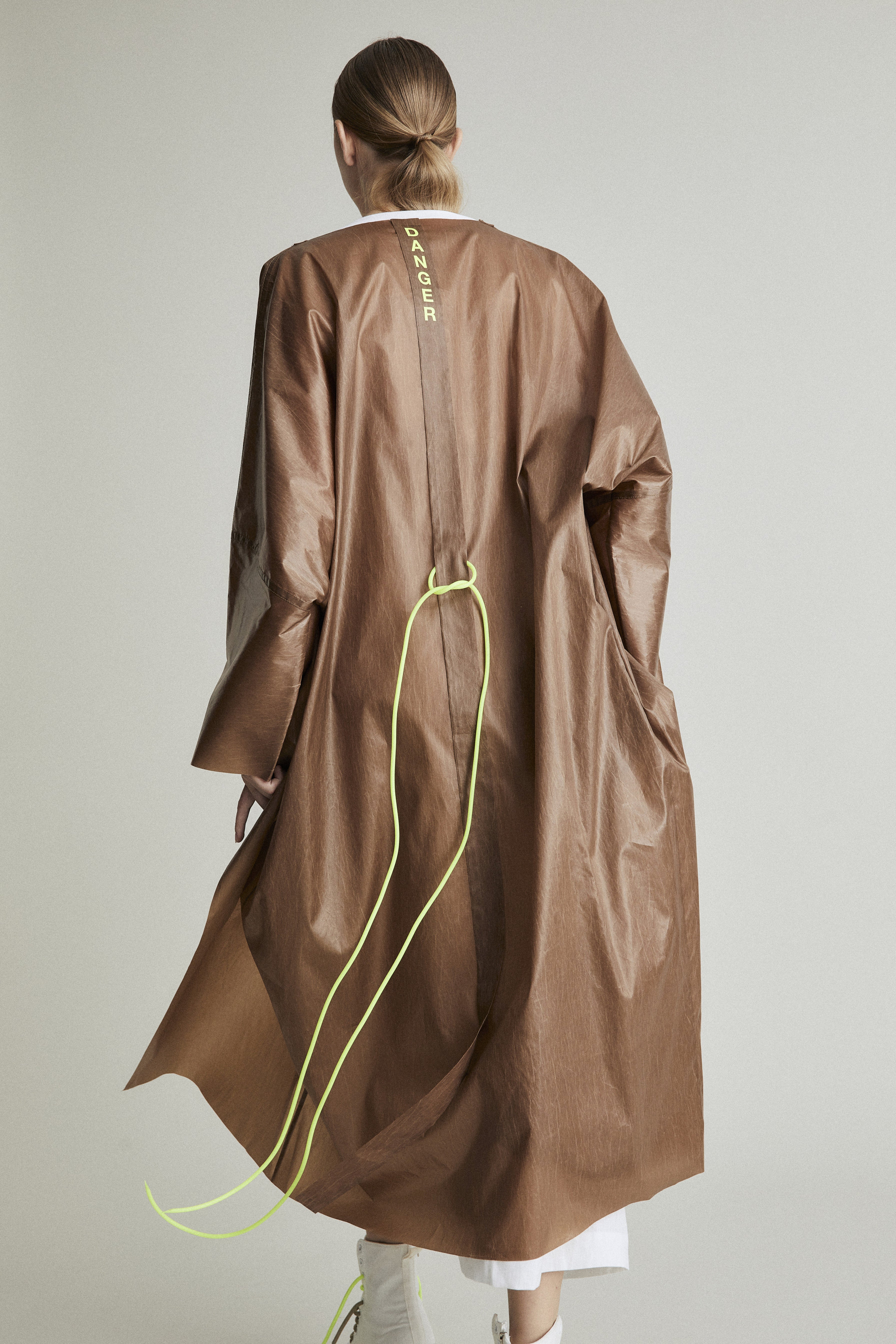 The back of a woman wearing alight raincoat bronze colored with bright green details. 
